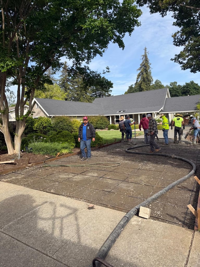 Community volunteer group working on driveway paving project at residential home with large trees and green lawn