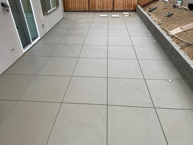 Newly poured concrete patio with grid scoring marks next to a house and wooden fence
